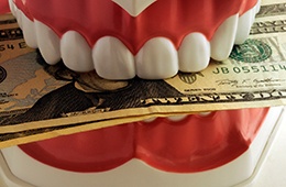 A closeup of model dentures biting dollar bills