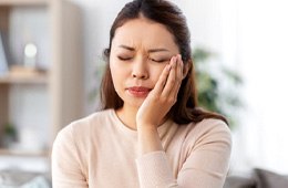 Woman on couch rubbing jaw due to tooth pain