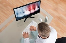 A dentist looking an x-ray on a monitor.