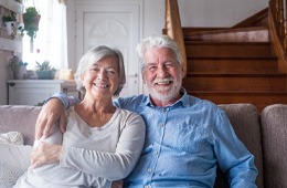 Older couple with dental implants in Campbell smiling on couch