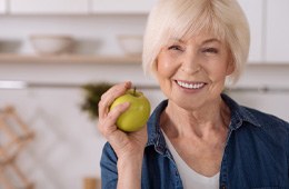 Woman with dental implants in Campbell smiling and holding apple
