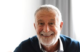 Senior man in blue shirt smiling with implant dentures in Campbell, CA