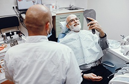 Senior man checking new implant dentures in mirror