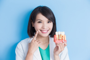 a person smiling and holding a model of dental implants
