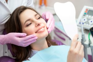 Woman with brown hair in dental chair looking at her teeth with tooth shaped mirror
