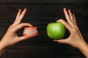 One hand holding a set of dentures while another hand holds an apple