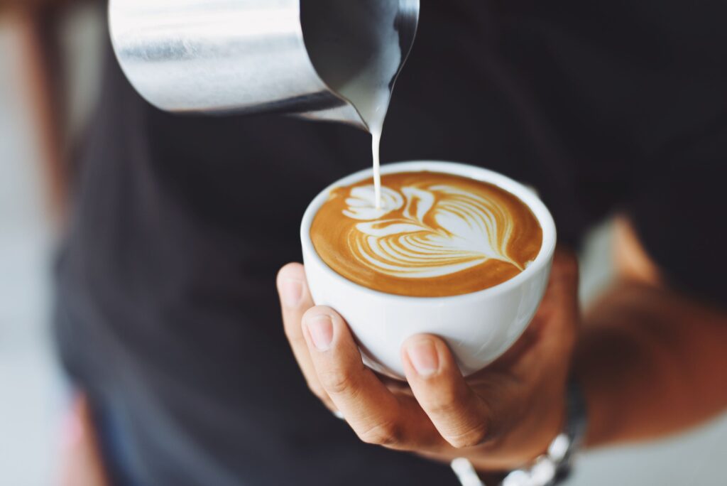Barista pouring decorative cream into cup of coffee